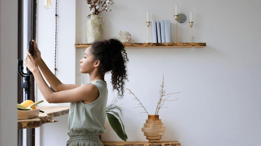 A woman using her smartphone on a tripod near a window in a bright room.