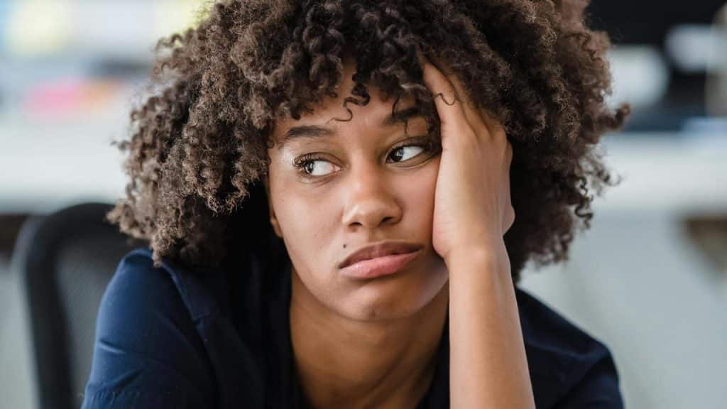 A woman with curly hair resting her head on her hand, looking bored.