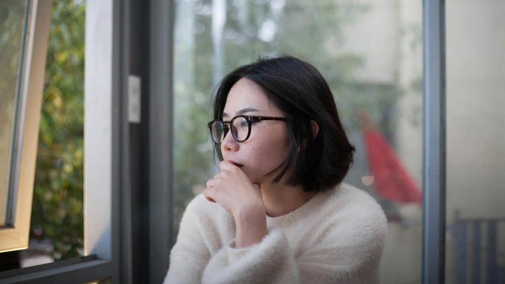 A woman with glasses gazing thoughtfully out a window.