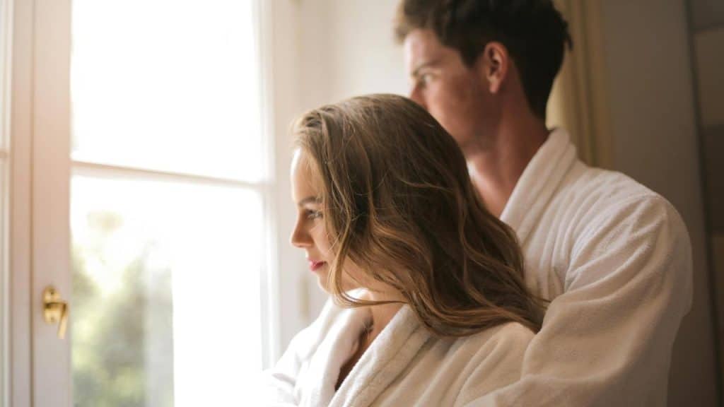 A couple in white robes standing by a window, looking outside.