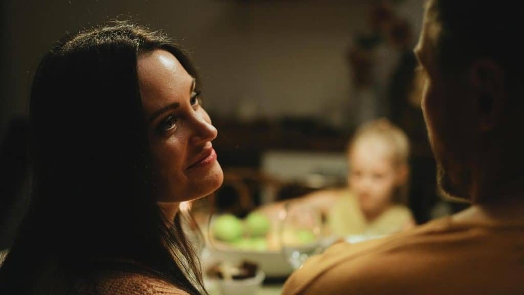 A woman gazing warmly at a man across the table while a child sits in the background.
