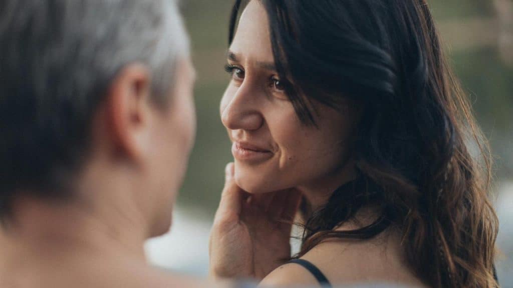 A woman smiling softly at a man as he gently touches her face.