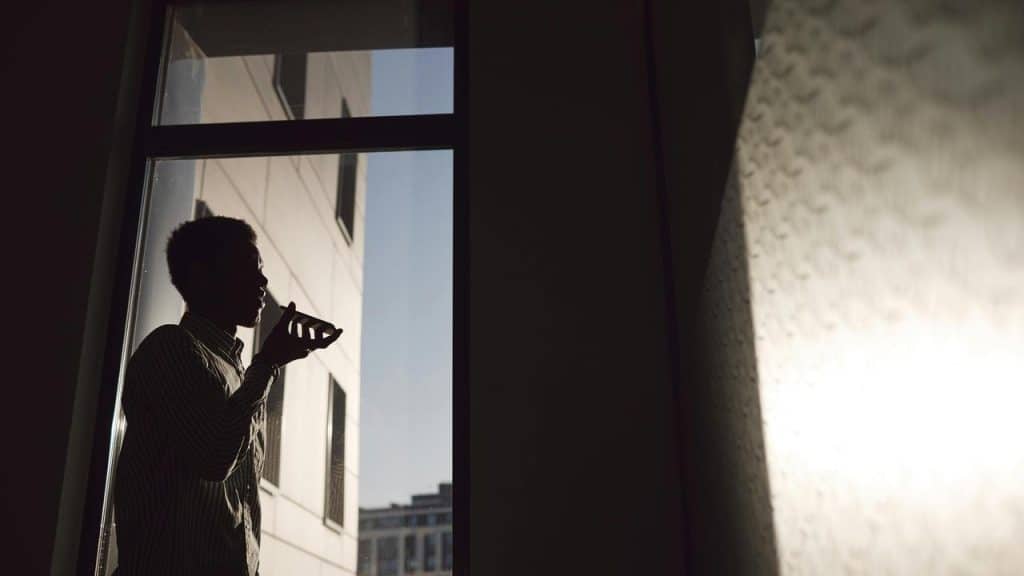 A silhouetted man speaking into a phone by a window at sunset.