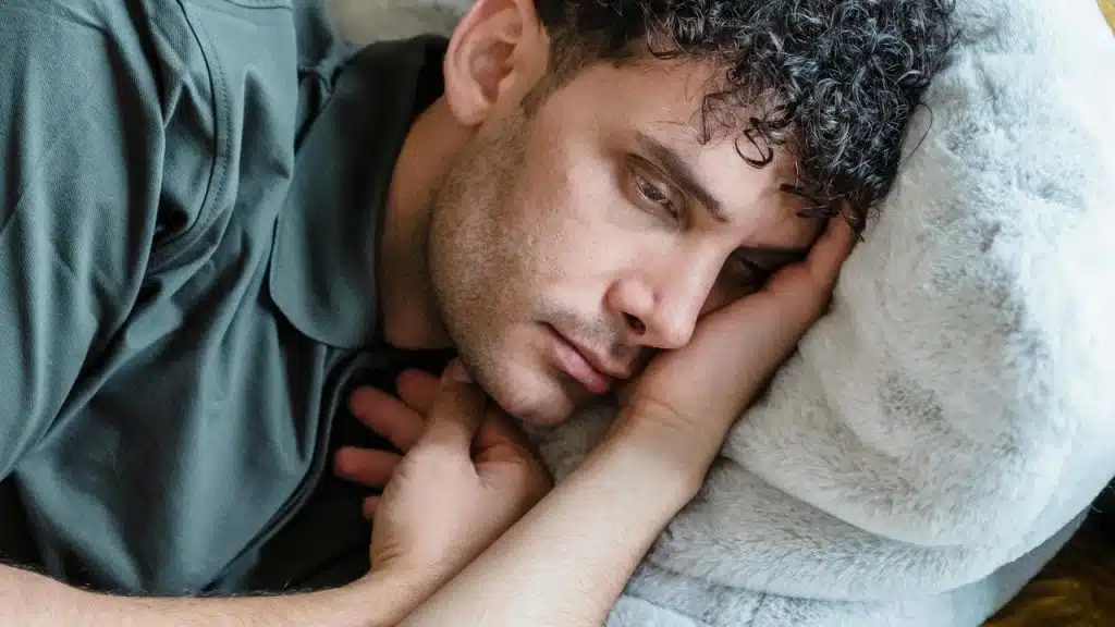 A pensive man lying on a couch with his head resting on his hand.