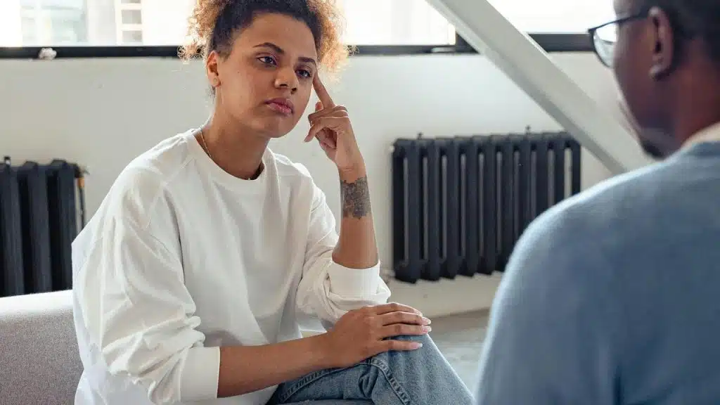 A woman listening thoughtfully to another person during a conversation indoors.