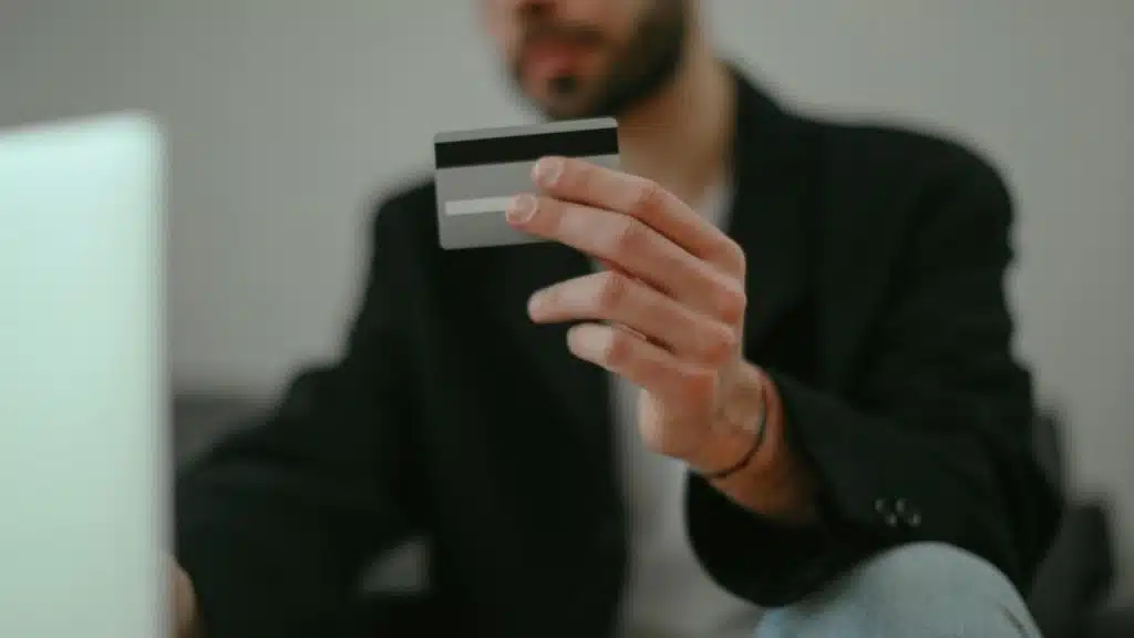 A man holding a credit card while using a laptop.