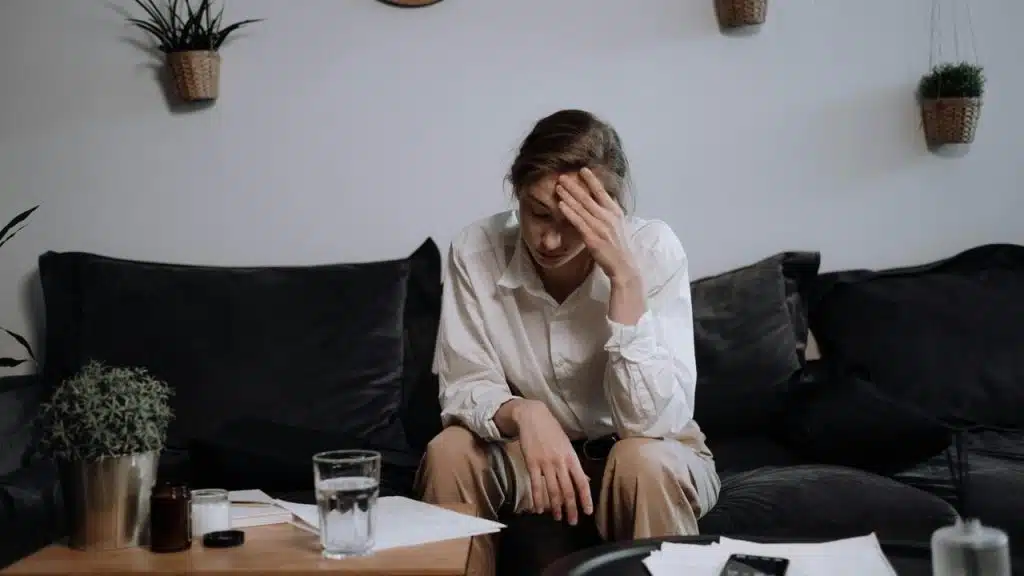 A stressed woman sits on a couch with papers on the table in front of her.