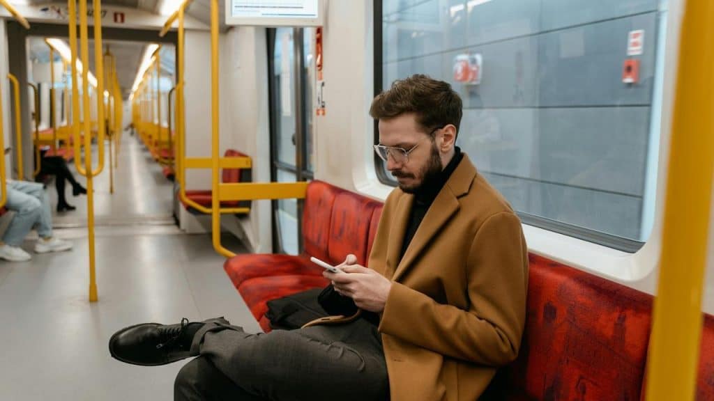 A man sits on a subway train looking at his phone.