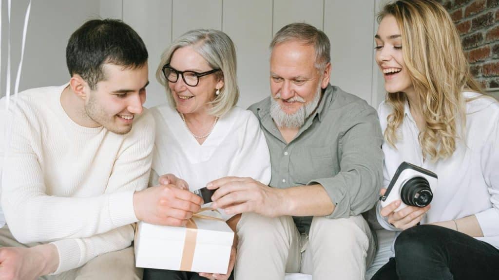 A family smiles together while opening a gift box at home.