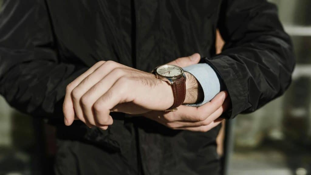 A man adjusts his wristwatch while wearing a jacket.