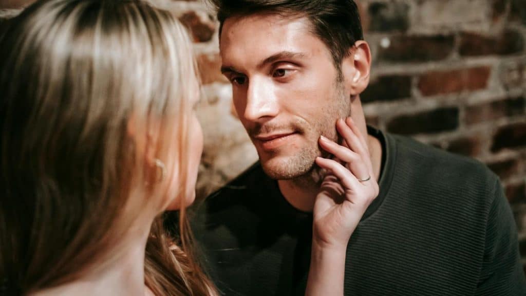 A couple gazes at each other closely, with the woman touching the man's face.