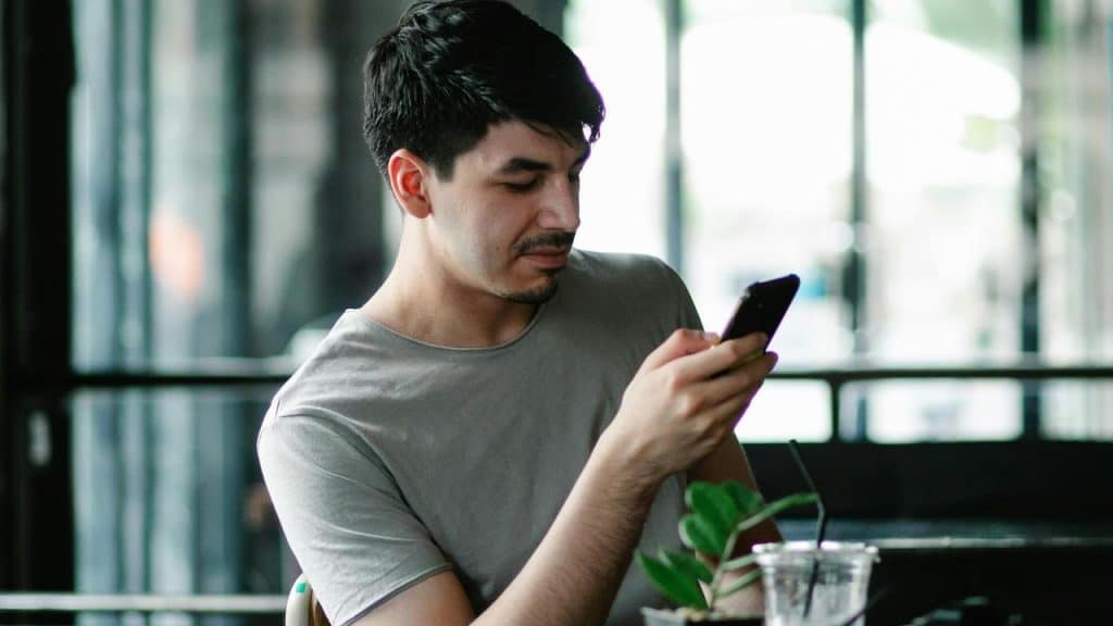 A man sits at a table looking at his smartphone.