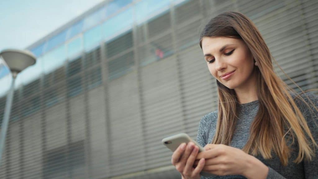 A woman stands outdoors looking at her smartphone.