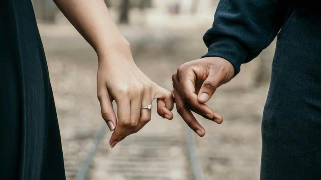 Two hands of different skin tones show pinky fingers locked over a blurred outdoor track.