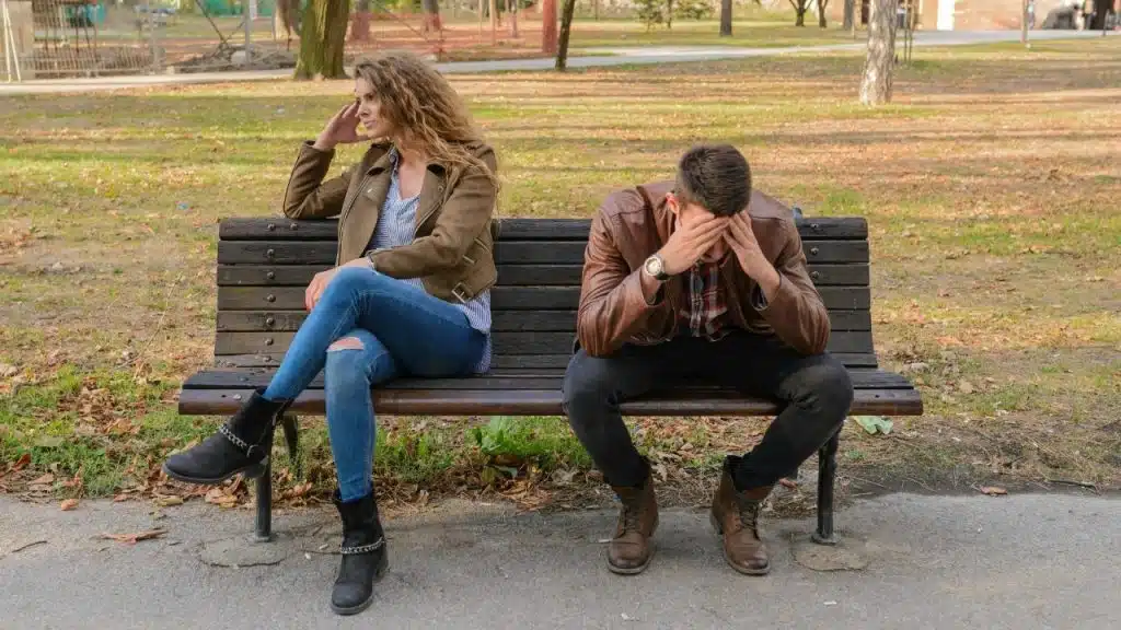 A woman and a man sit on a park bench facing away from each other.