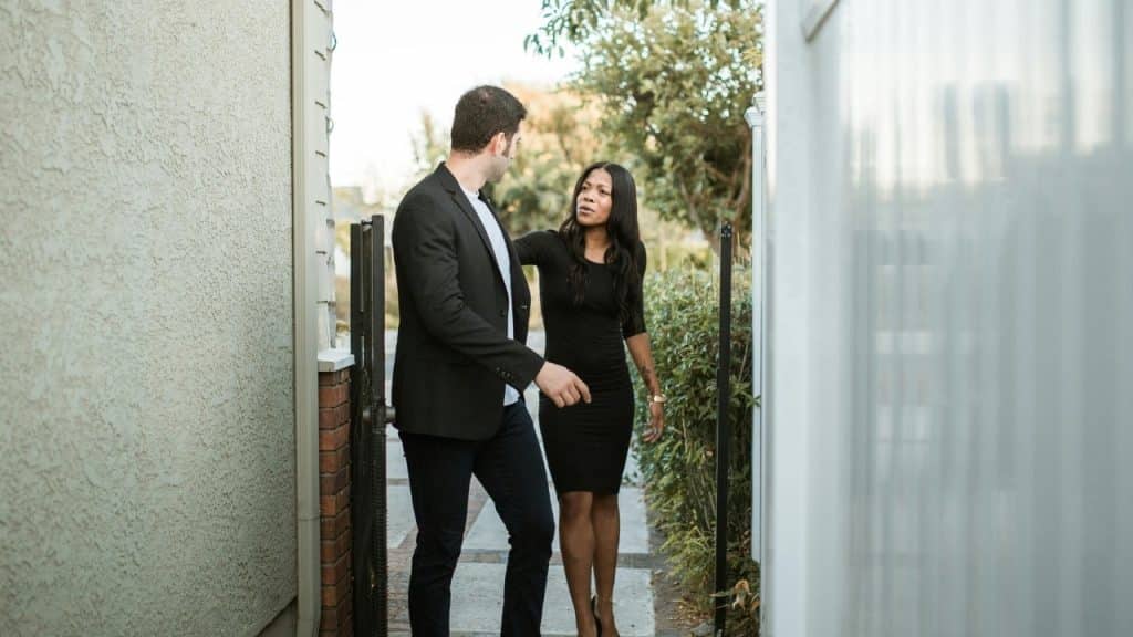 A man in a blazer walks toward a gate while a woman speaks to him.