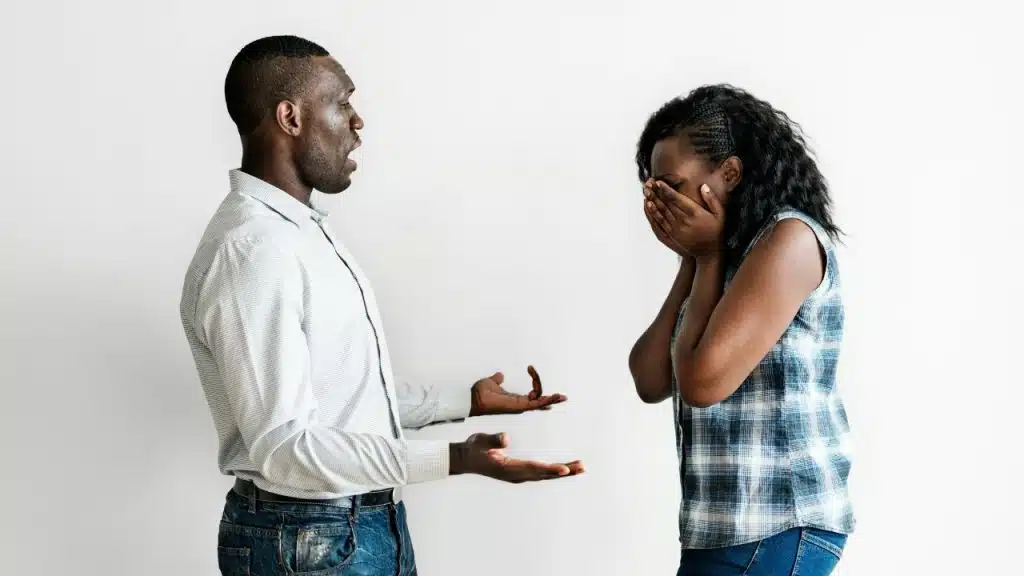 A man gestures with open palms toward a woman who is covering her face.