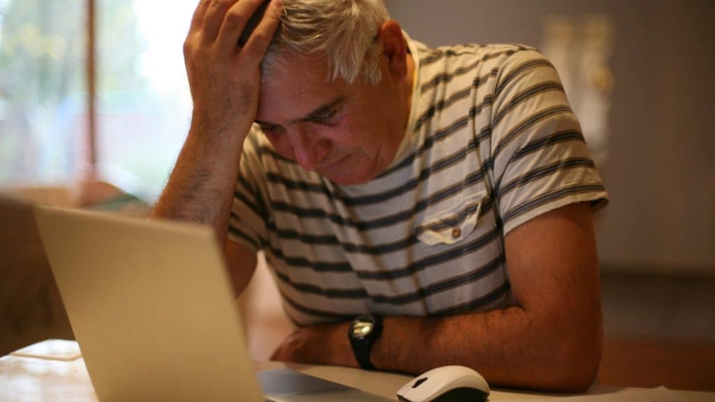 A man with grey hair rests his head in his hand while looking at a laptop.