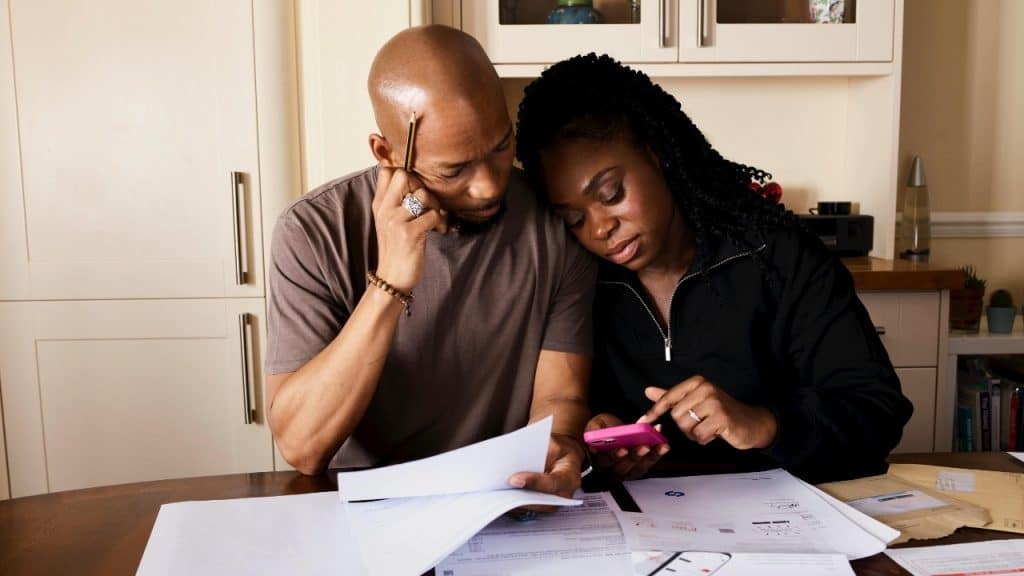 A man and woman sit at a table reviewing paper documents and a pink mobile phone.