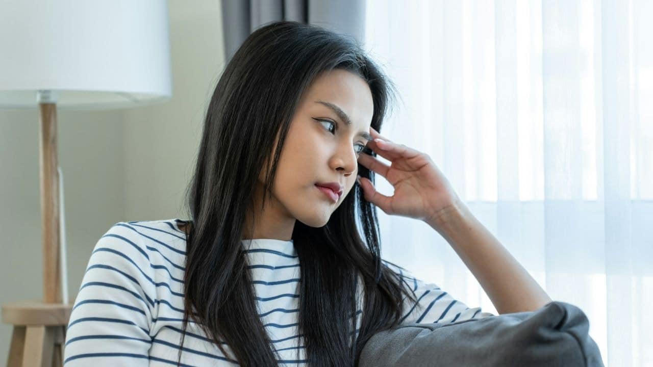 A woman in a striped shirt sits on a couch and gazes out a window.