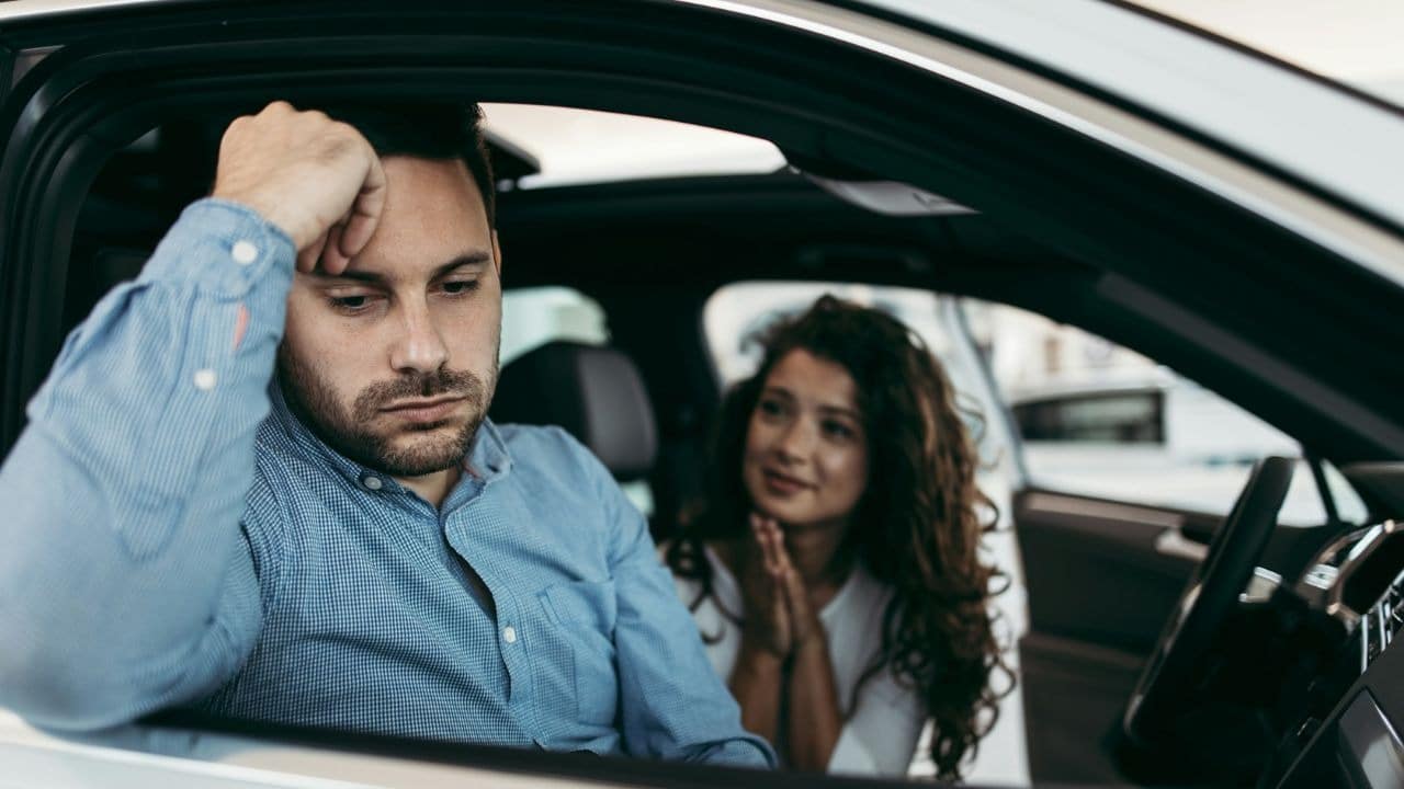 A man leans against a car window while a woman holds her hands together.