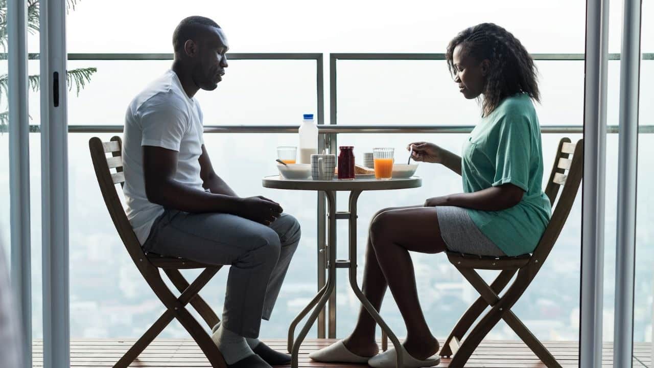 A man and woman sit at a small table on a balcony eating breakfast together.