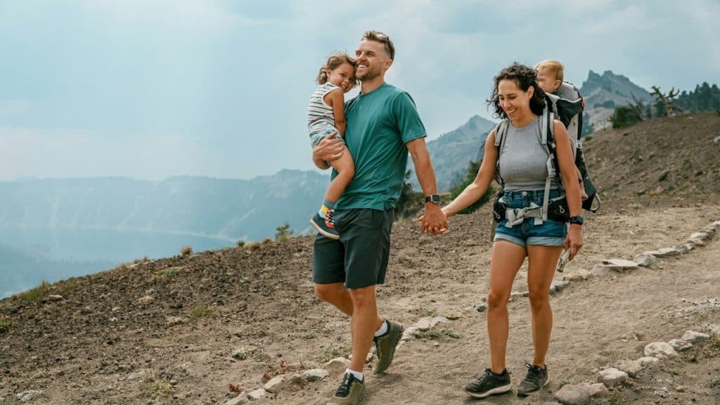 A couple walking down a trail while carrying their children and holding hands.