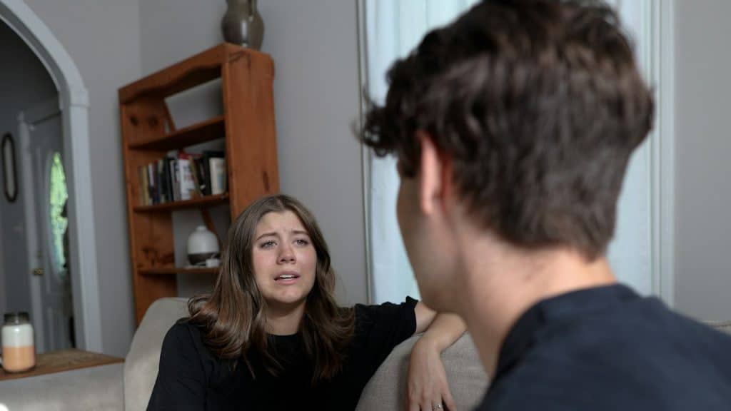 An upset woman talking to man sitting on a couch with her.