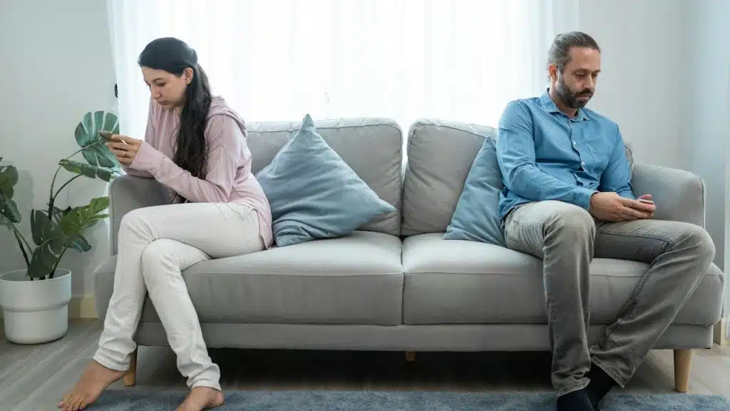 A couple sitting apart from each other on a couch and using their smartphones.