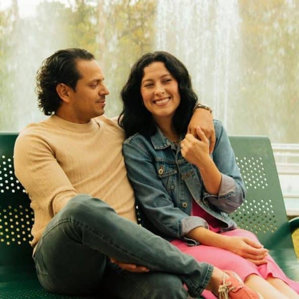A couple sits on a bench in front of a fountain.