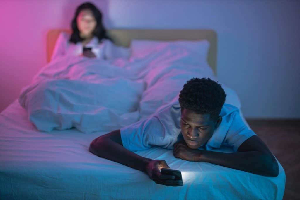 A man and woman at bed and using their phone