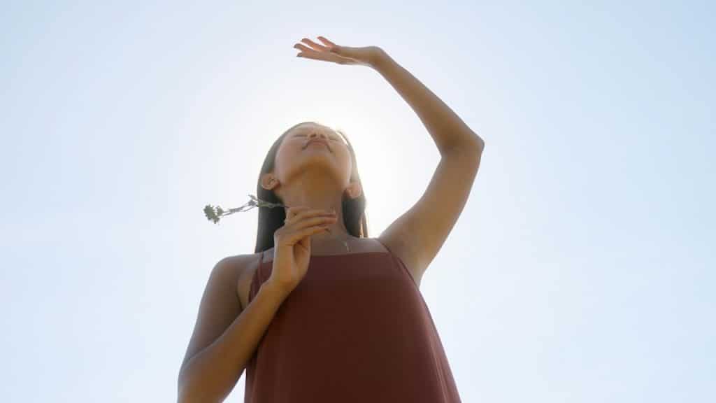 A woman holding a flower is standing under the sky at daytime.