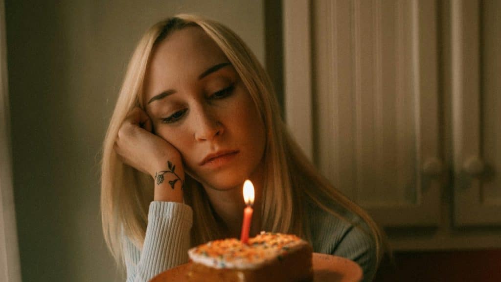 A sad woman holding a cake is sitting indoors.