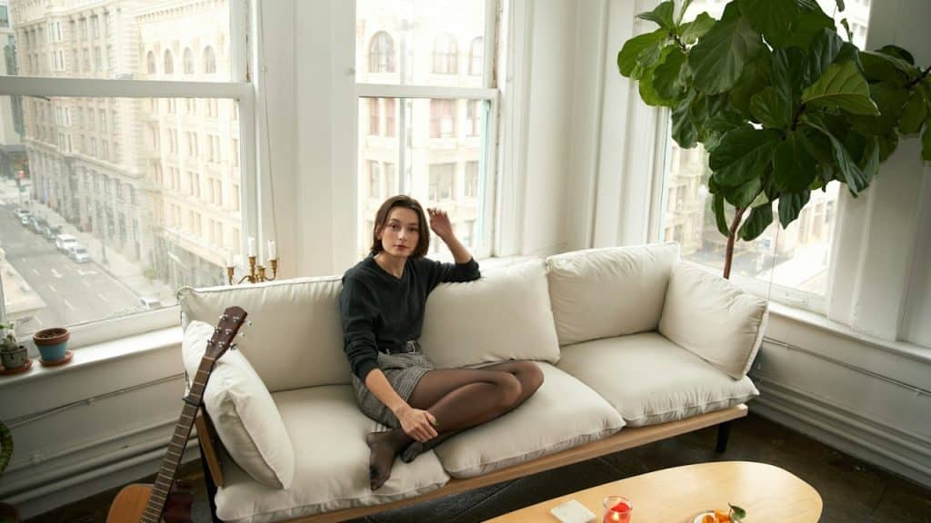 A woman sitting on a sofa near a big window.