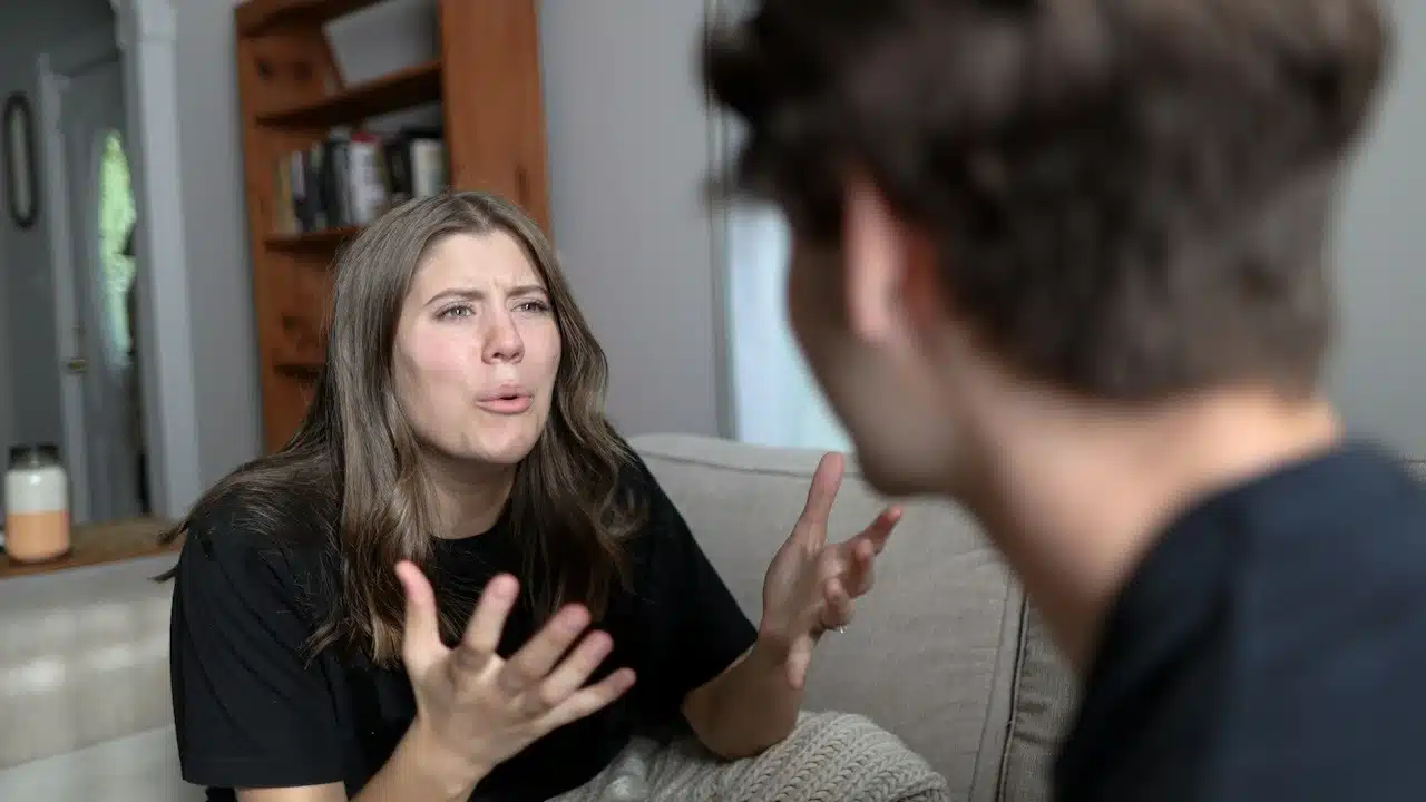 A woman arguing with her husband while sitting on a sofa next to him.