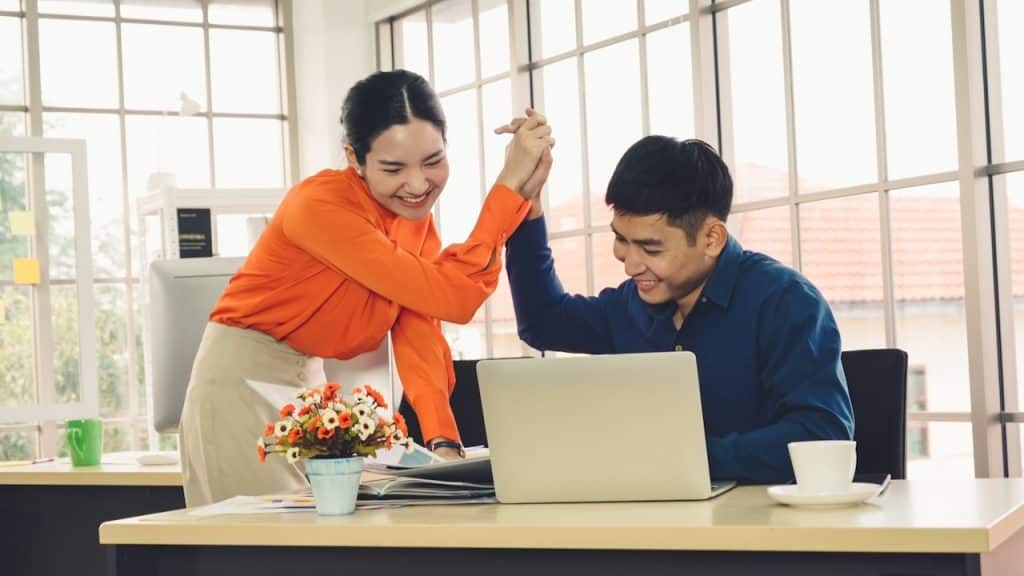 A couple giving a high five while sitting at a table in an office.