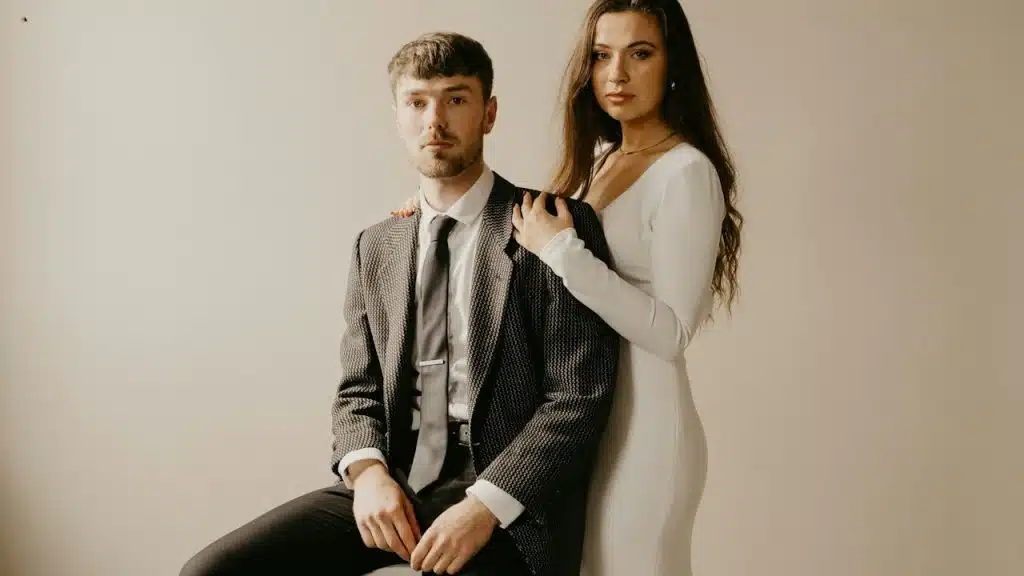 A woman resting her hands on a sitting man’s shoulders while she stands behind him.