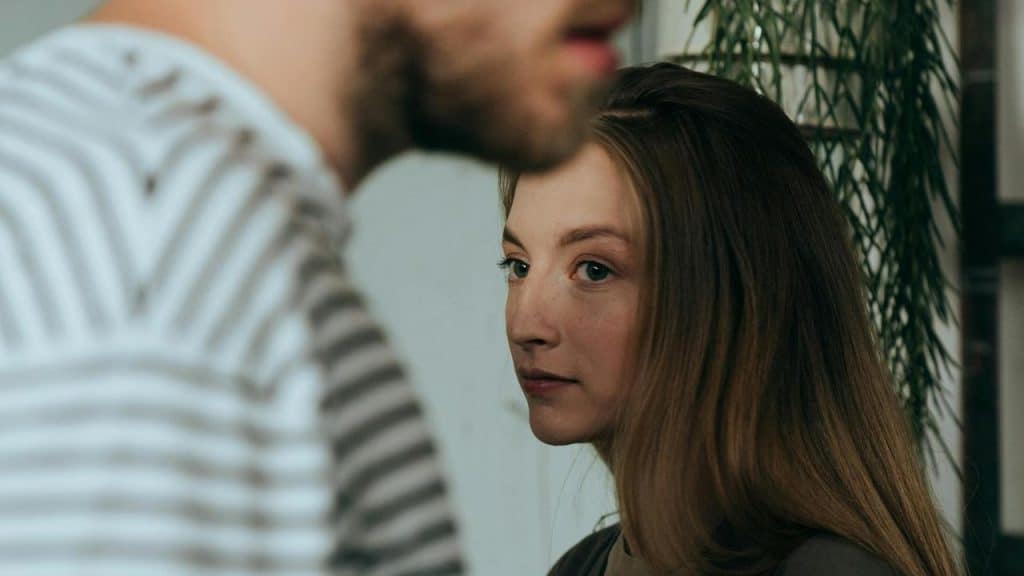 A woman looking sideways with a serious expression while a man stands near.