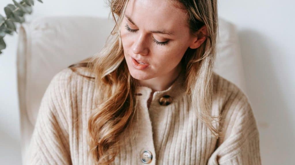 A woman looking down with a thoughtful expression while sitting indoors.