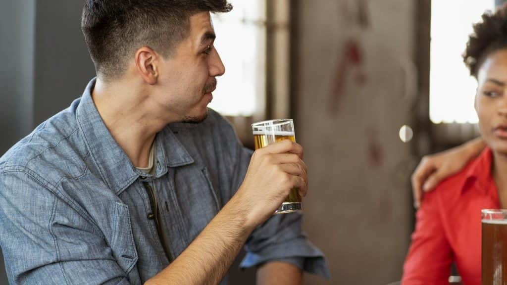 A man holding a glass of beer while talking to a woman sitting beside him.