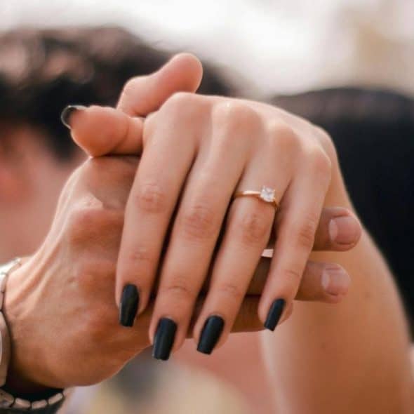 A close-up of a couple holding hands with an engagement ring visible.