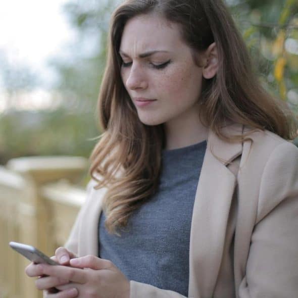 A young woman looking at her phone while standing outdoors by a railing.