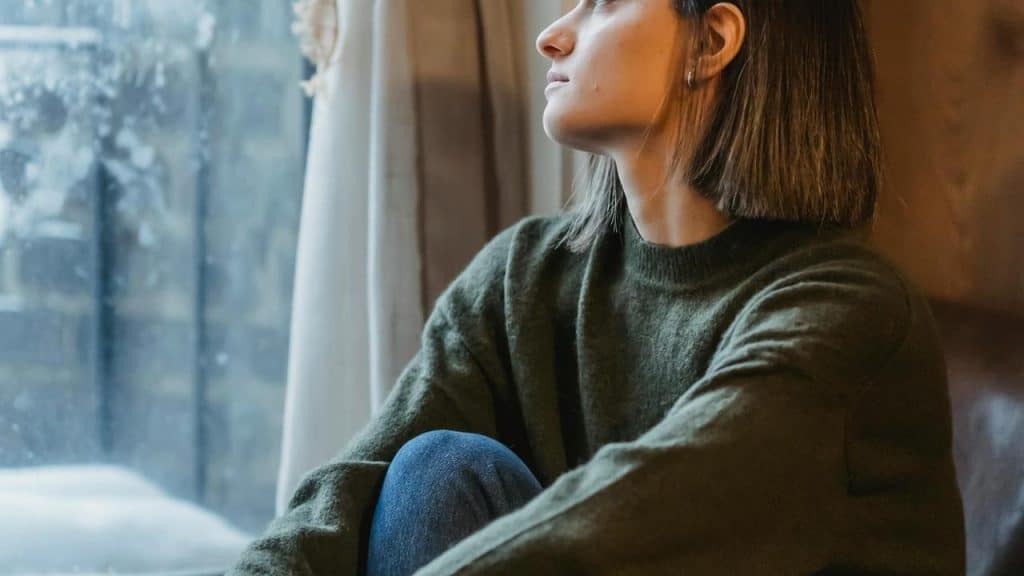 A woman in a green sweater sitting by a window and looking outside.