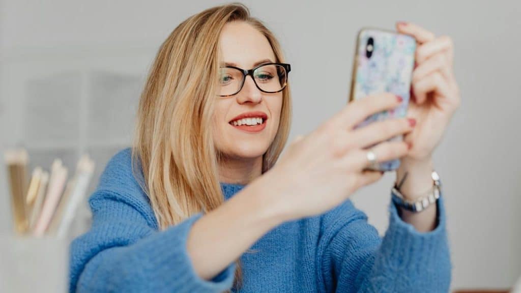 A woman wearing glasses taking a selfie with her smartphone.