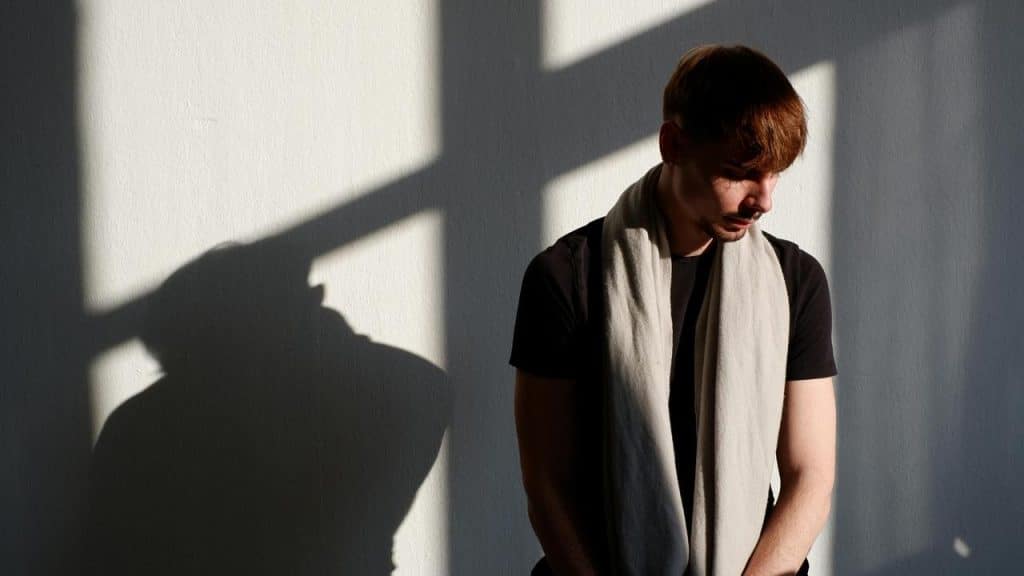 A man standing in sunlight against a wall, looking down with a shadow cast beside him.