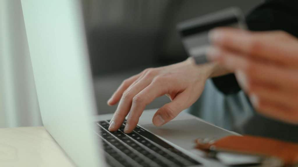 A person typing on a laptop while holding a credit card.