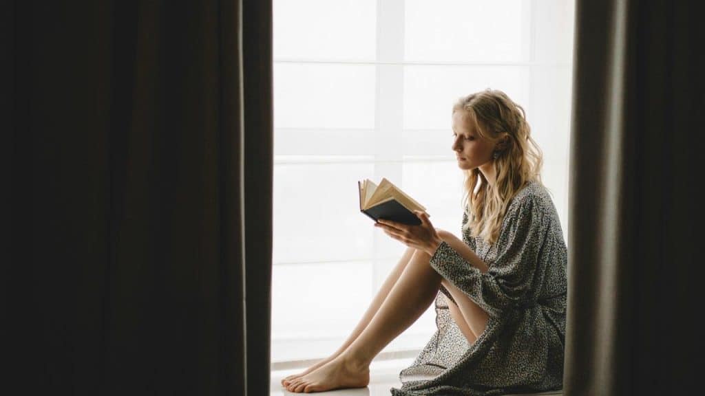 A woman sitting by a window reading a book.