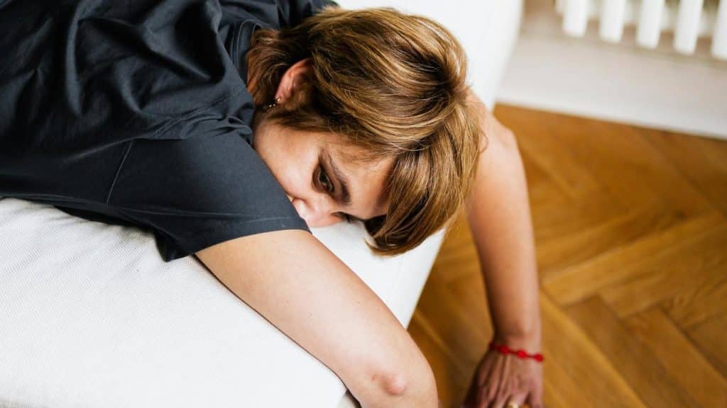 A tired woman leaning over the edge of a couch with her arm hanging down.