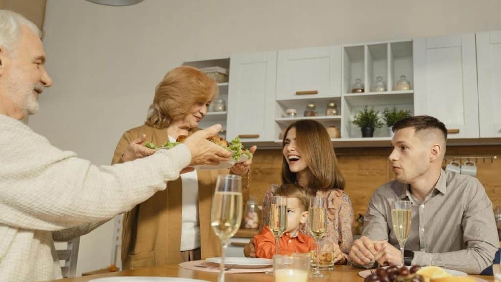 A family gathered around a table while an older woman serves food.