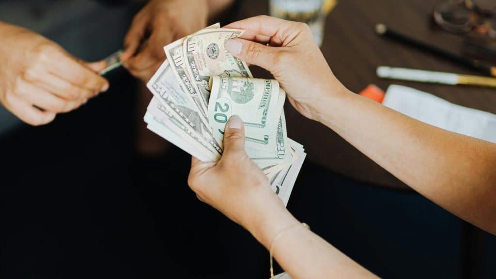 A person holding a stack of dollar bills while making a payment.